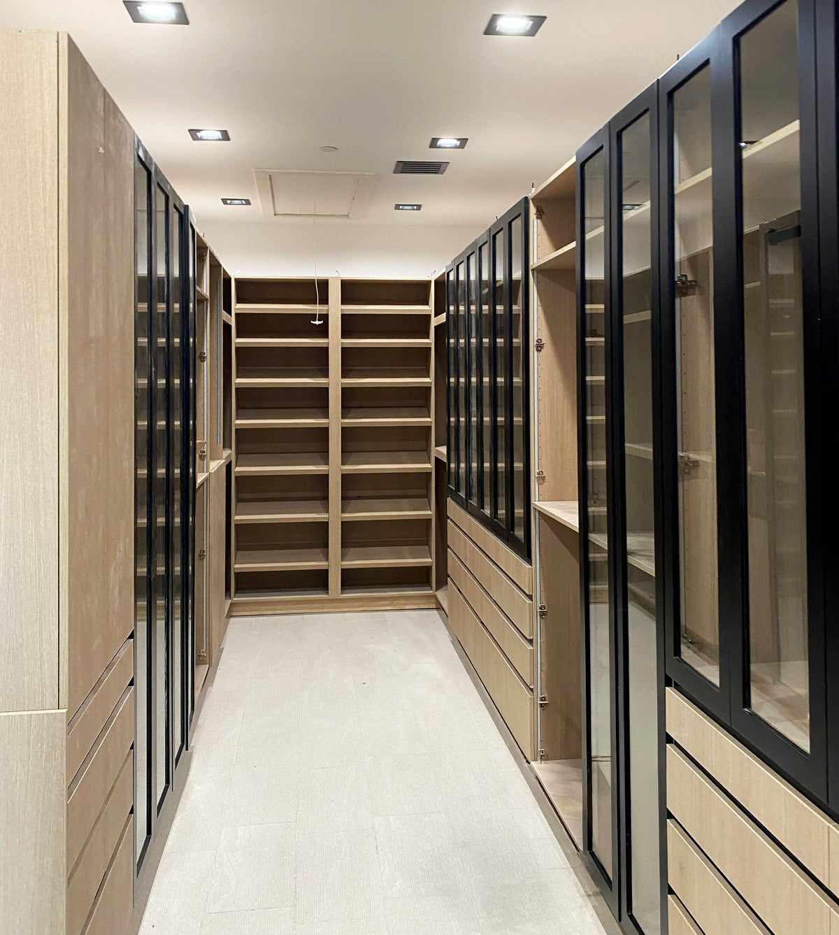 Walk-in closet with glass-front storage cabinets, drawers and open shelving by Gentry Stinson