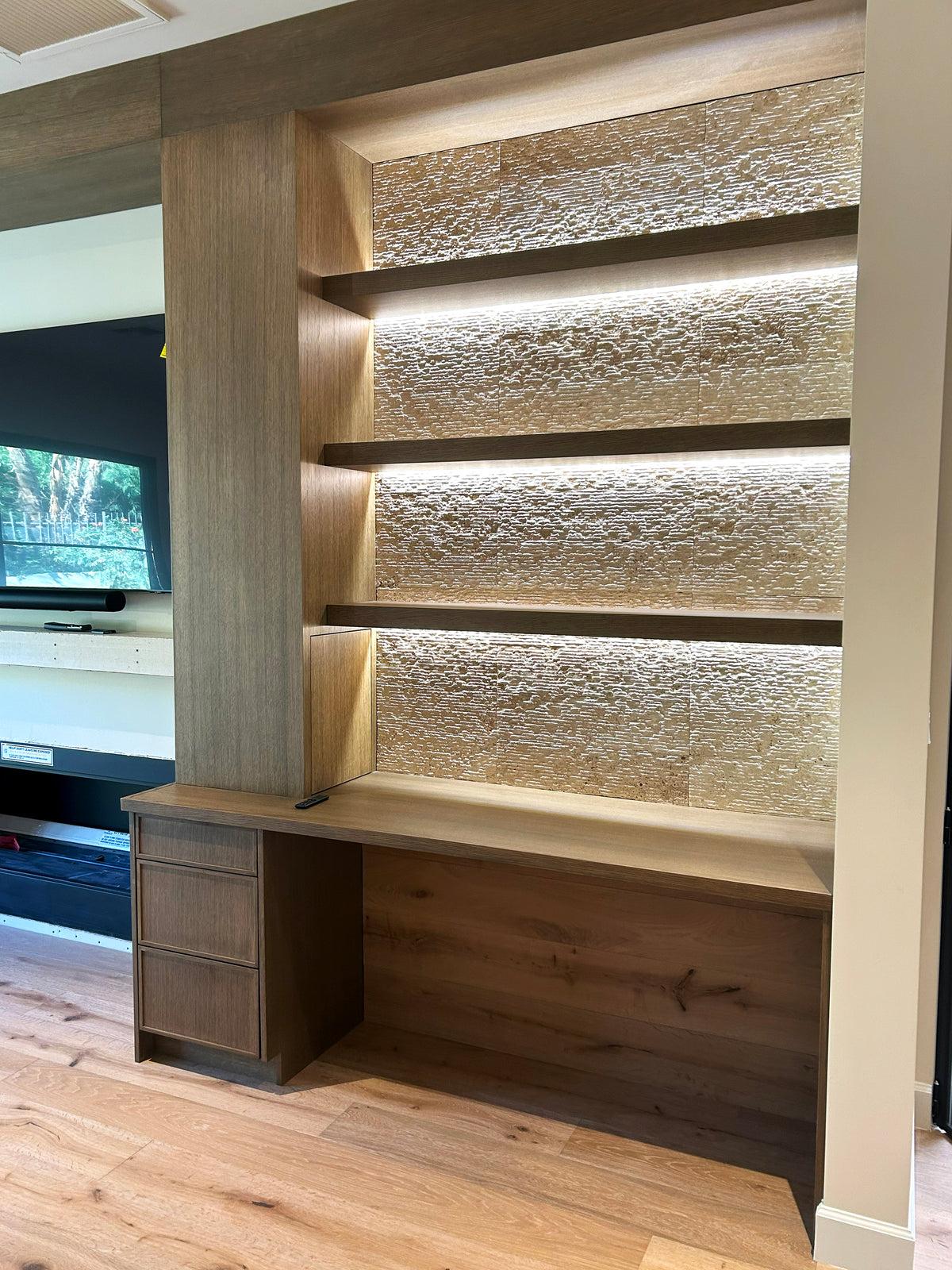 Illuminated built-in shelving above a wood desk and drawer cabinet by Gentry Stinson